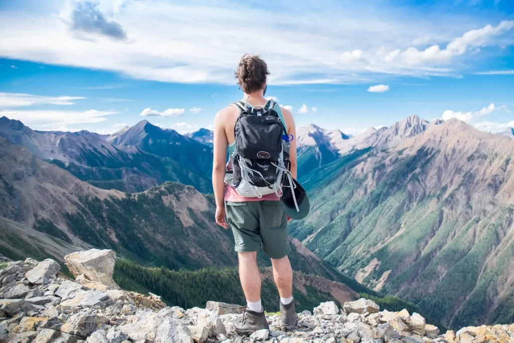 A young boy is looking towards the mountain with a camping backpack.